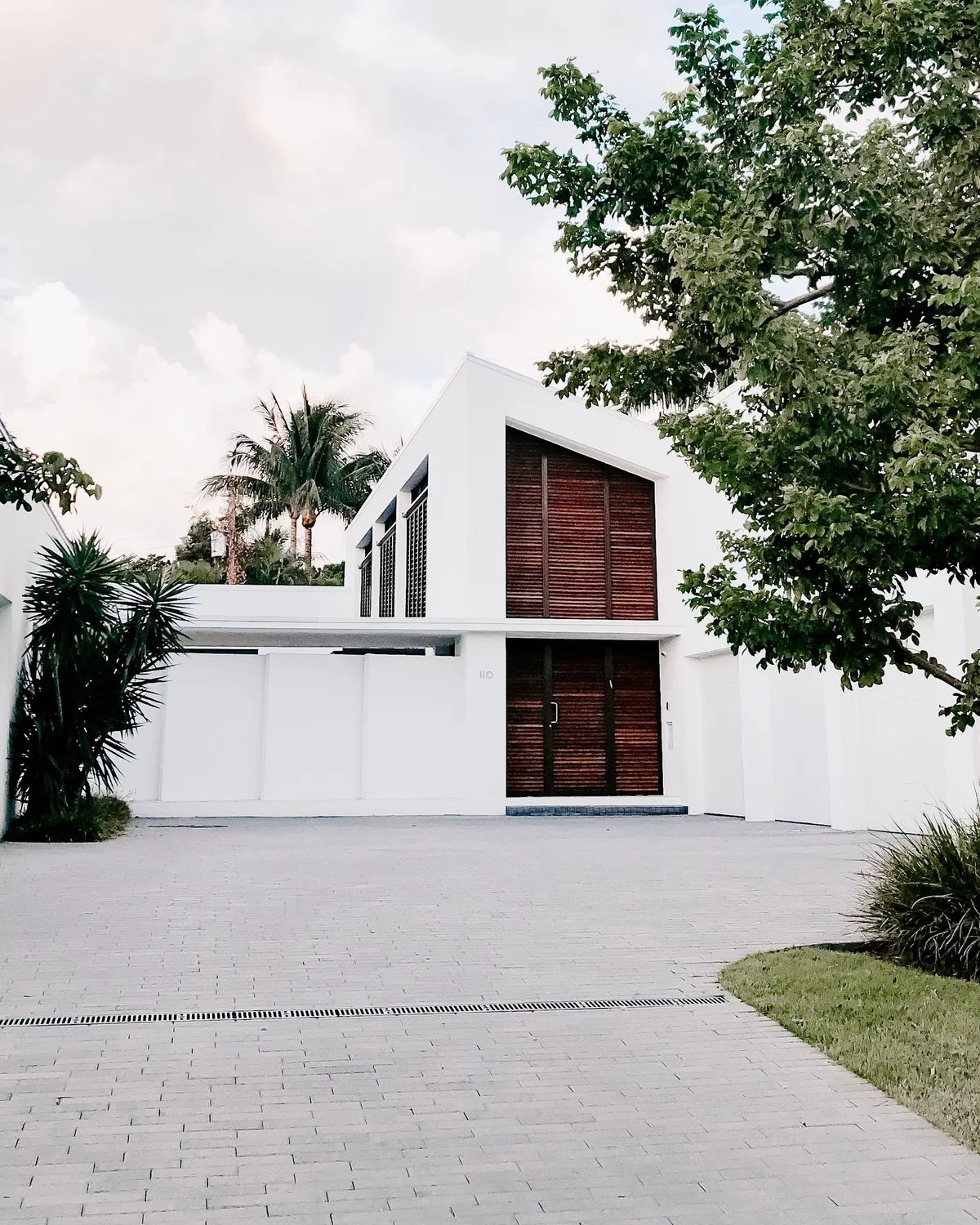 Maison contemporaine à enduit blanc, persiennes de bois et toit à pente unique, sous les palmiers